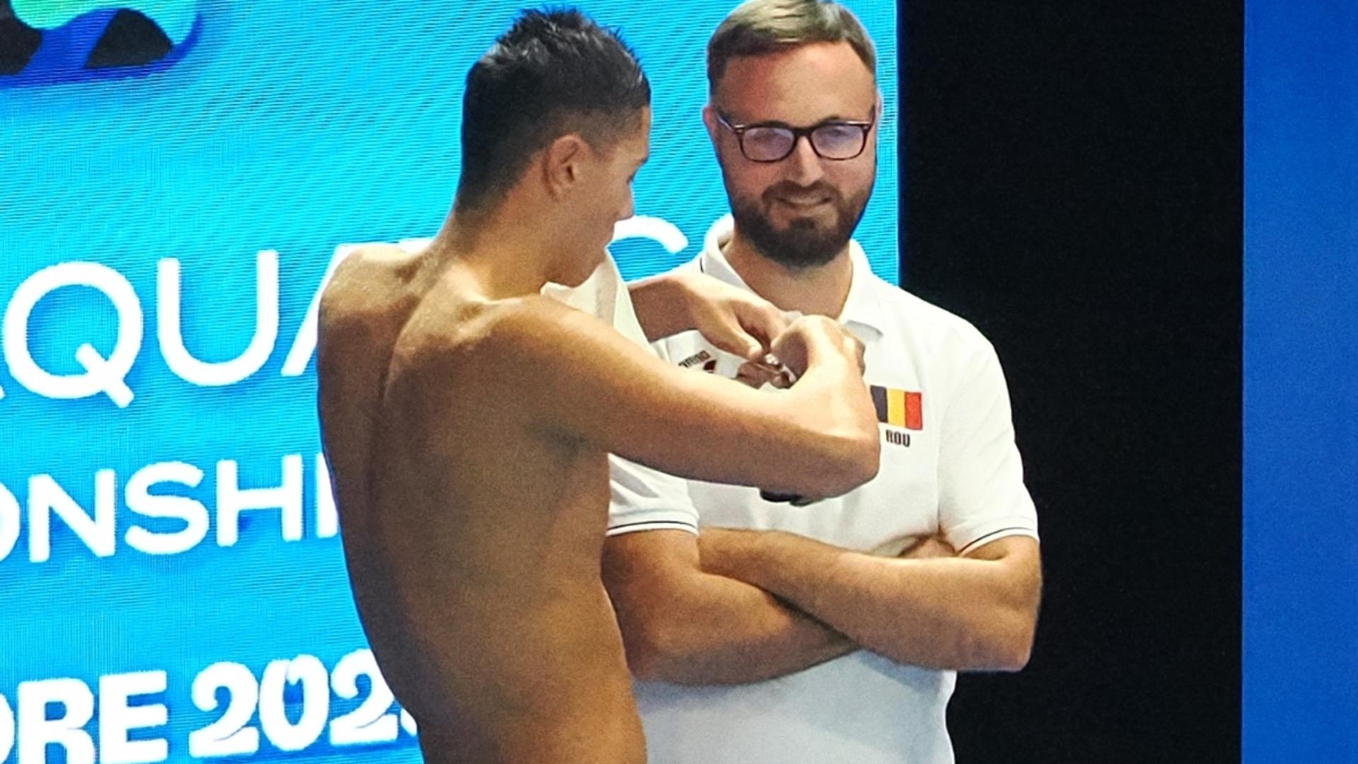 David Popovici în costum de înot la startul unei curse, antrenorul Adrian Rădulescu observând în fundal record european înot stabilit. | sursa foto: Gazeta Sporturilor